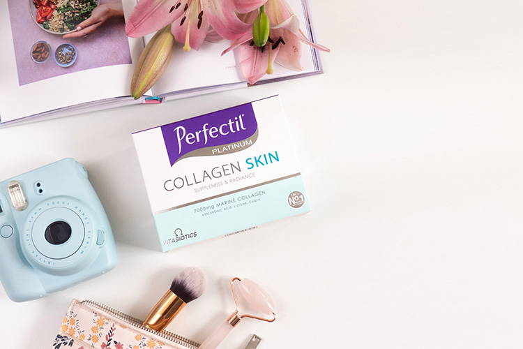 Perfectil Collagen Skin Drink Product Packshot On A White Background Next To Camera, Makeup Bag/Brushes, Flowers & Book