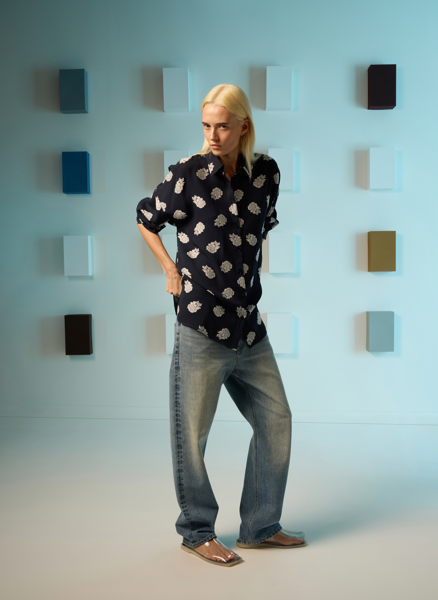 Model wearing a patterned shirt and baggy jeans against a colorful background.