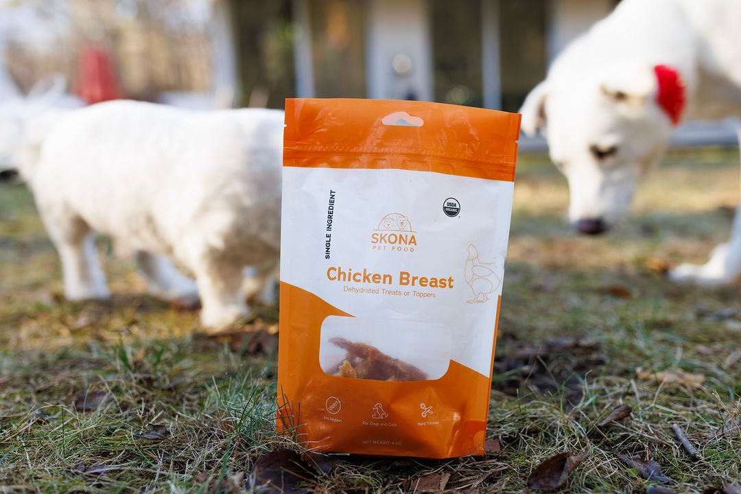 A package of chicken treats with two dogs in the background.
