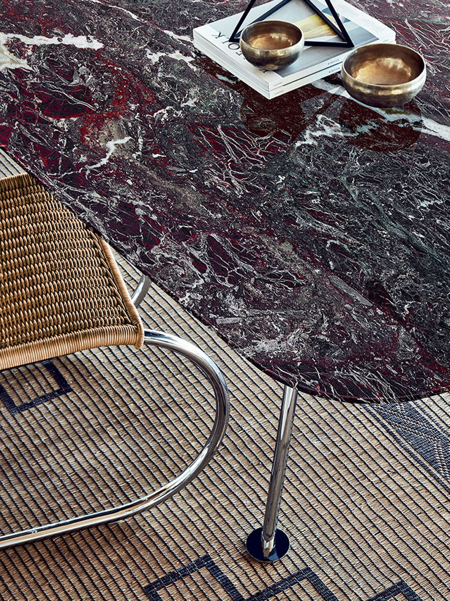 A Knoll marble table with a woven chair on a patterned rug.