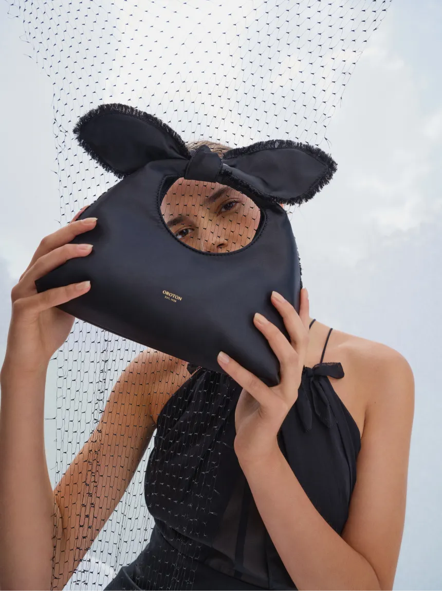 A person holding a black handbag with a bow against a dotted backdrop.