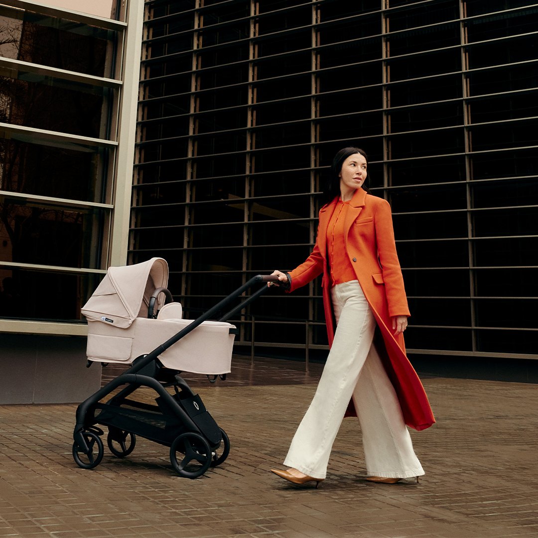 Woman in orange coat walking with a stroller in an urban setting.