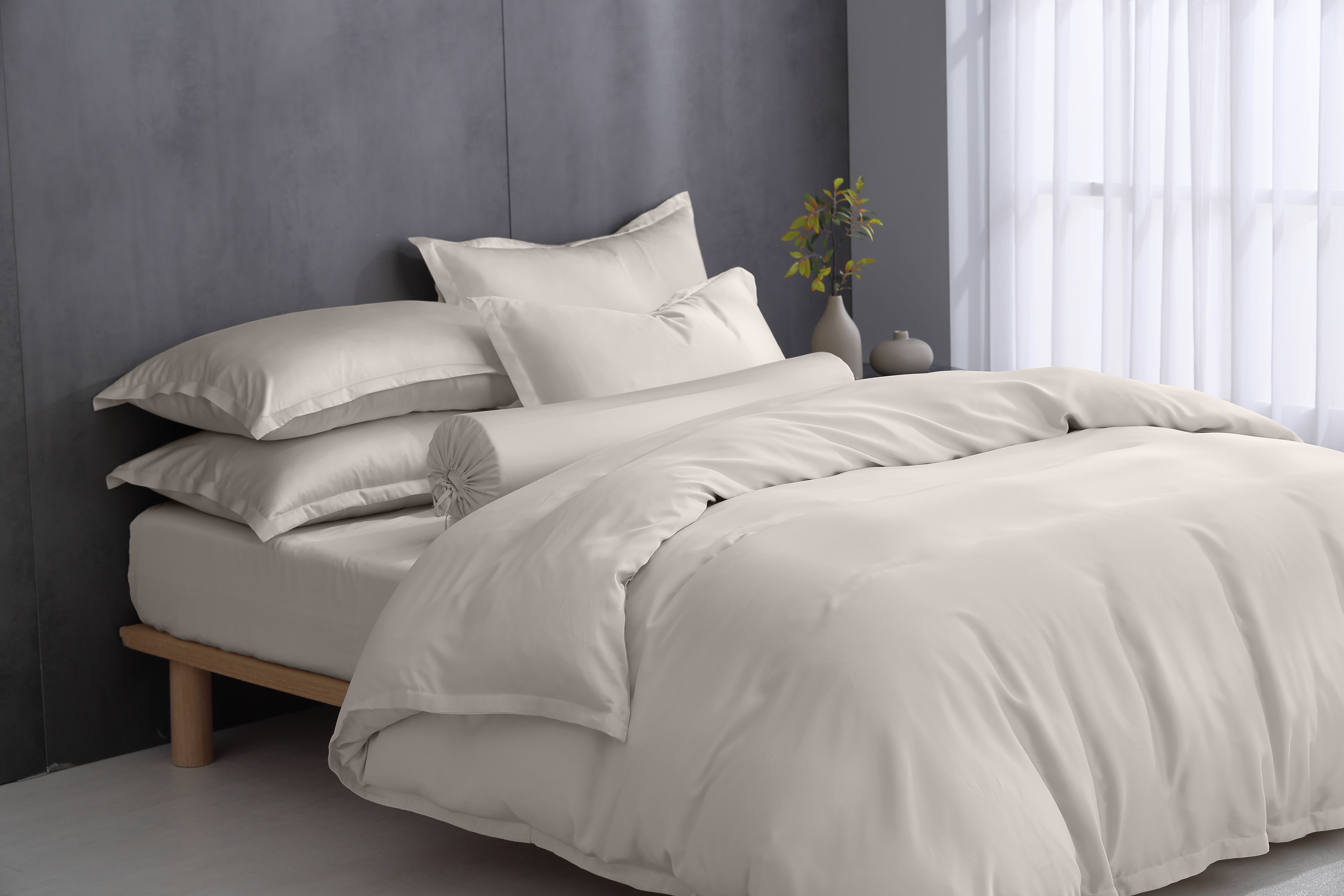 Cozy bed with beige bedding against a gray wall and natural light.