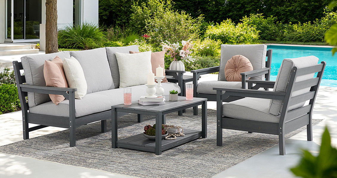 Outdoor seating area with gray furniture, cushions, and a coffee table by a pool.
