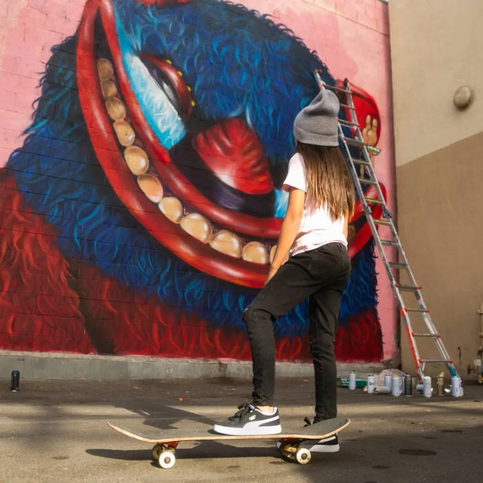 girl on skateboard looking at wall mural wearing puma