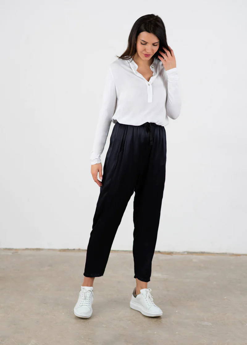 A model wearing a white, long sleeved top with blue black satin trousers and white trainers
