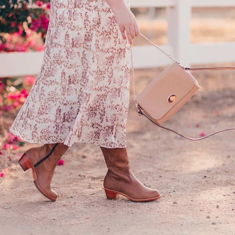 Woman wearing tan leather Condesa wide calf boots with a floral midi skirt and crossbody bag, walking outdoors.