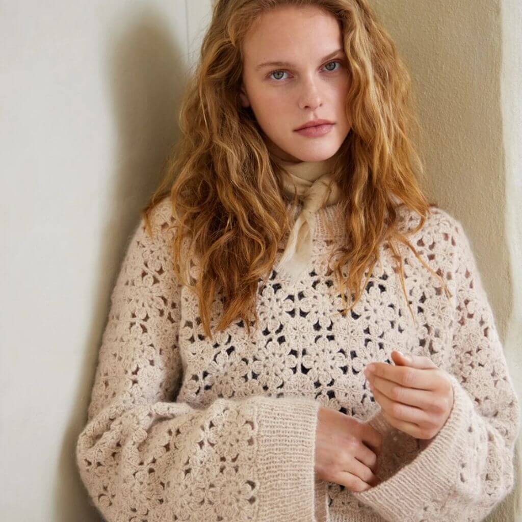 Frau in einem beigen Pullover mit Blumenmuster.