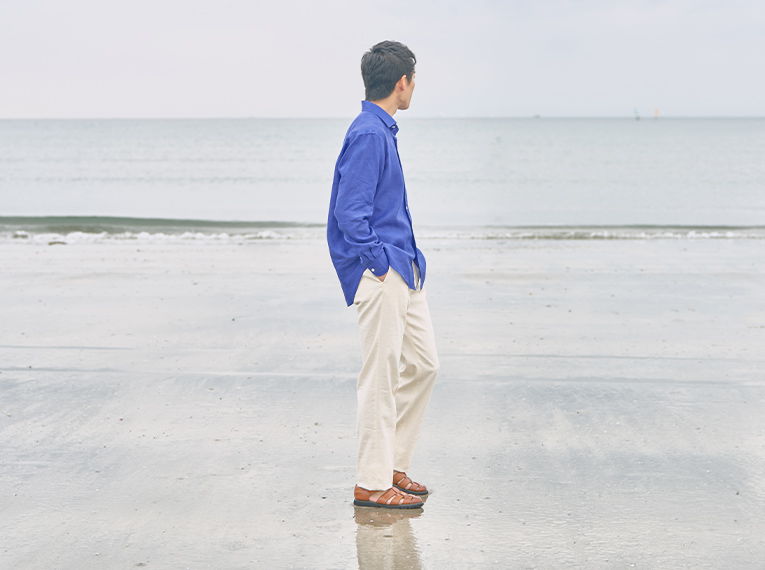 Person in blue shirt standing by the ocean on a cloudy day.