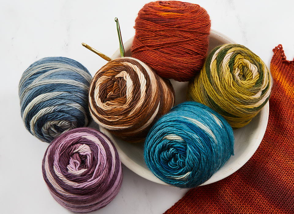 Colorful Herrschners Be-Drifty yarn balls arranged in a white bowl on a table.