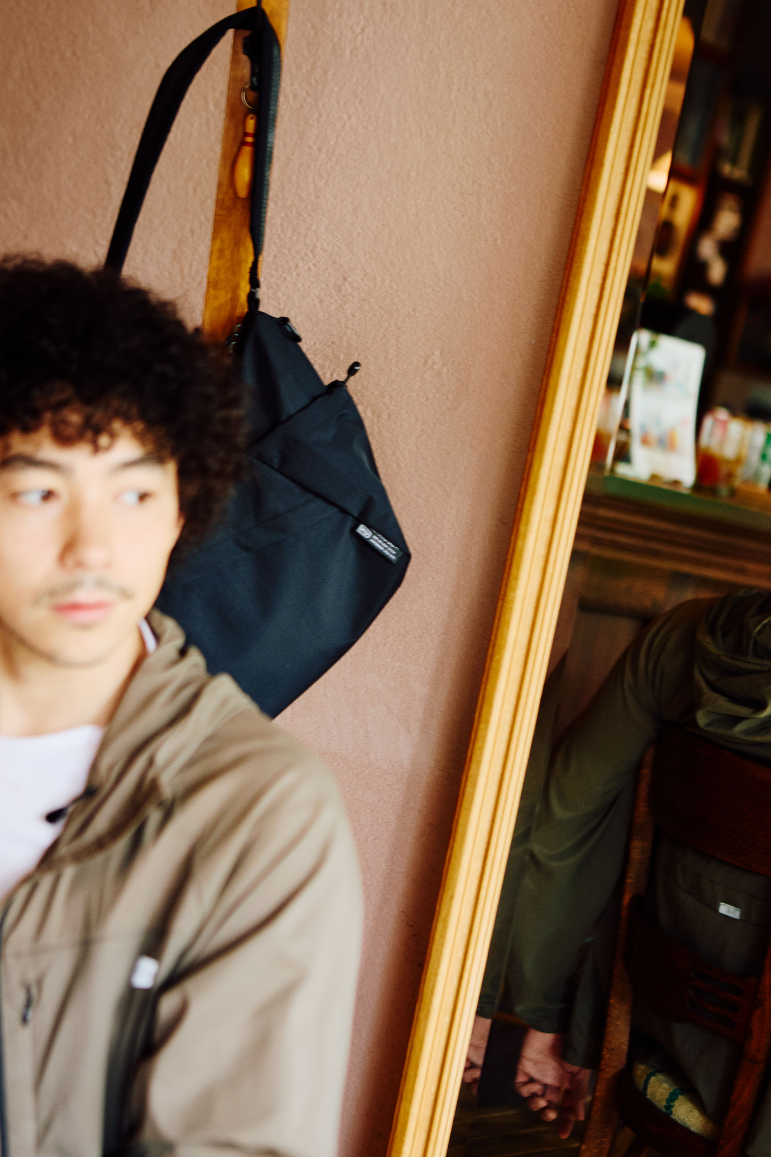 Young man with curly hair next to a mirror, reflecting another person.