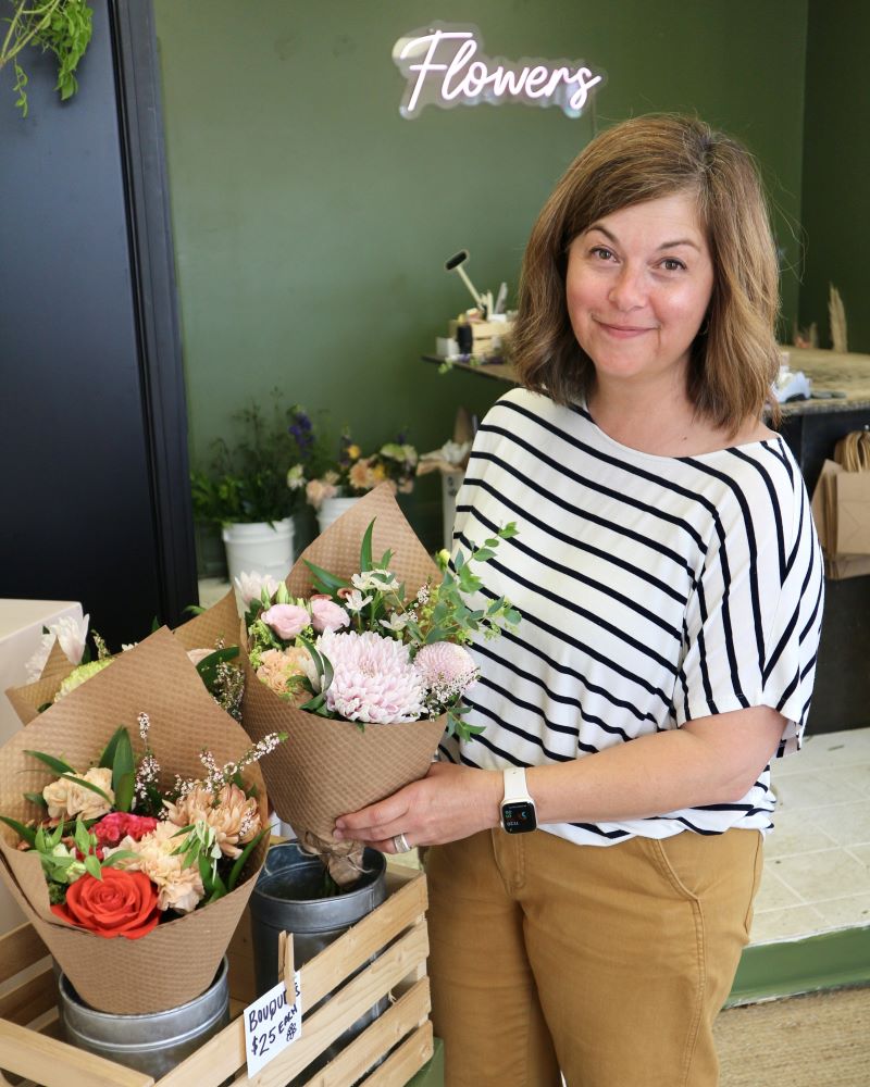 Woman holding flower bouquets in a shop with a green wall.