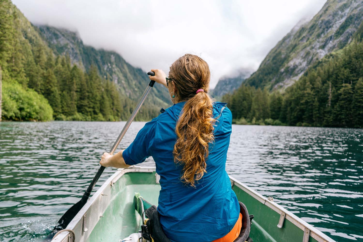 Person kayaking on a lake surrounded by mountains and trees.