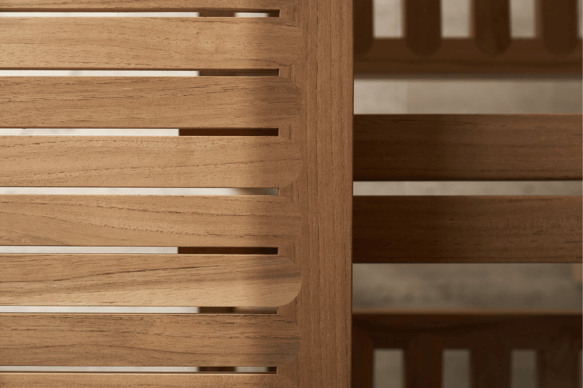 A close up of teak outdoor furniture with curved wood slats.