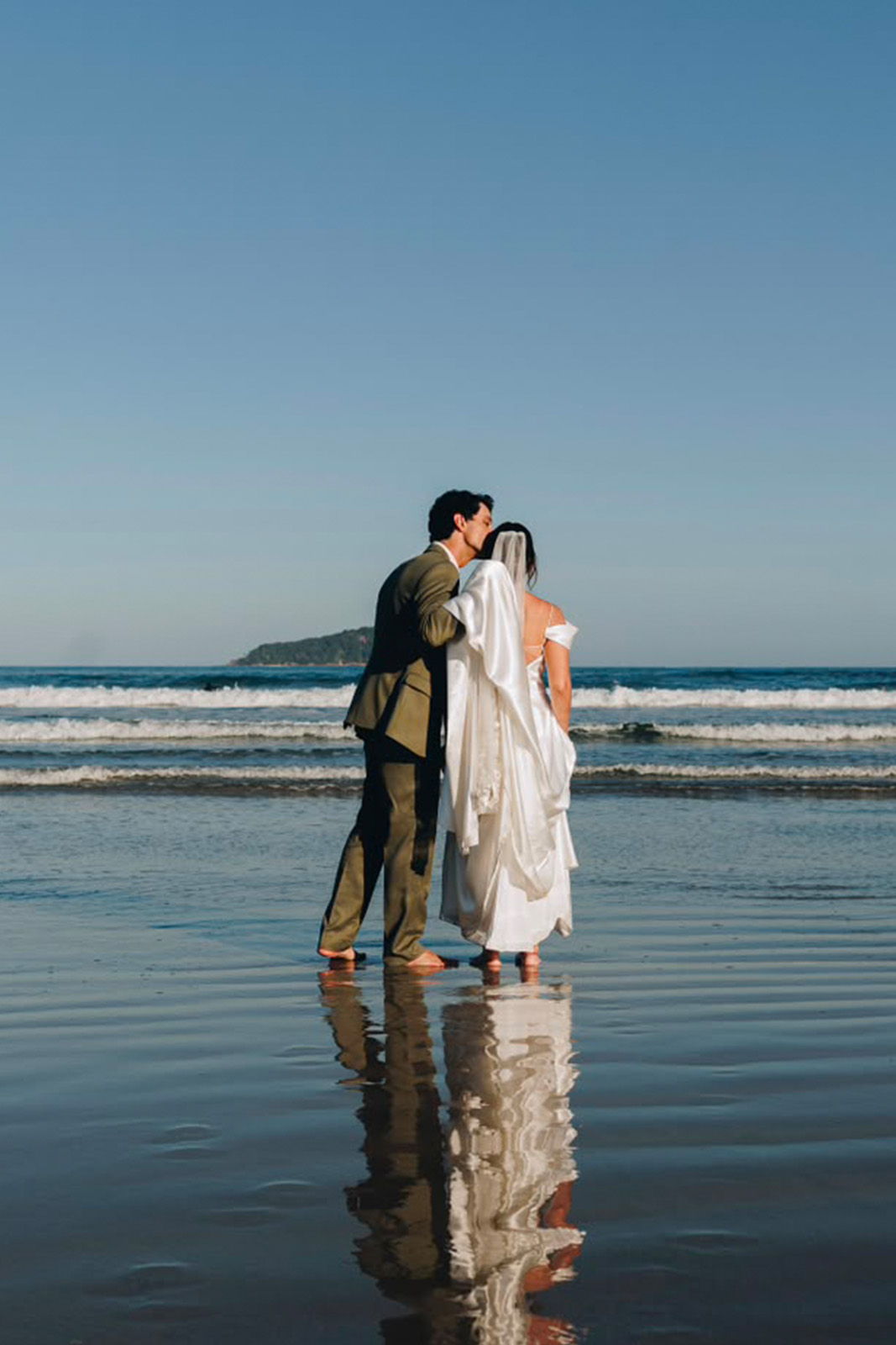A couple kissing on a beach, with waves and reflections in the water.