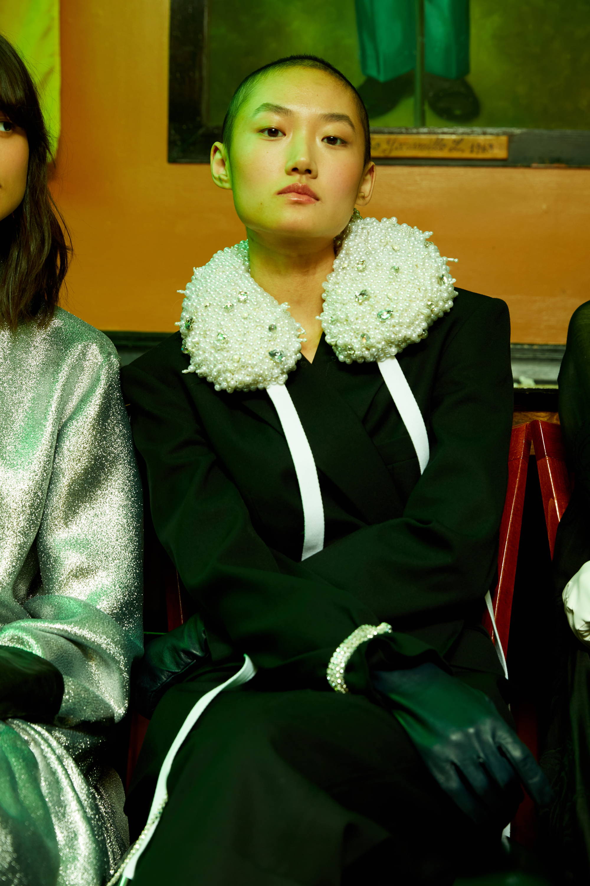 A model in a black outfit with a floral collar sitting among others.
