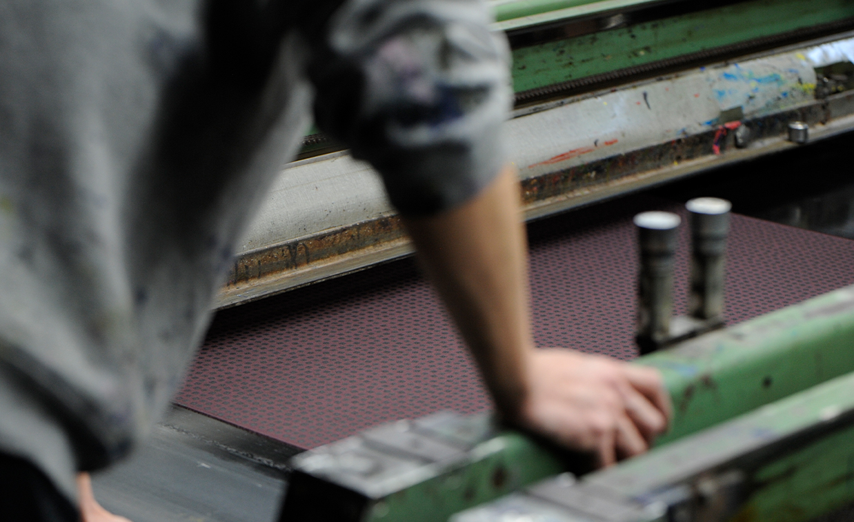 Person operating a printing press with a maroon surface.