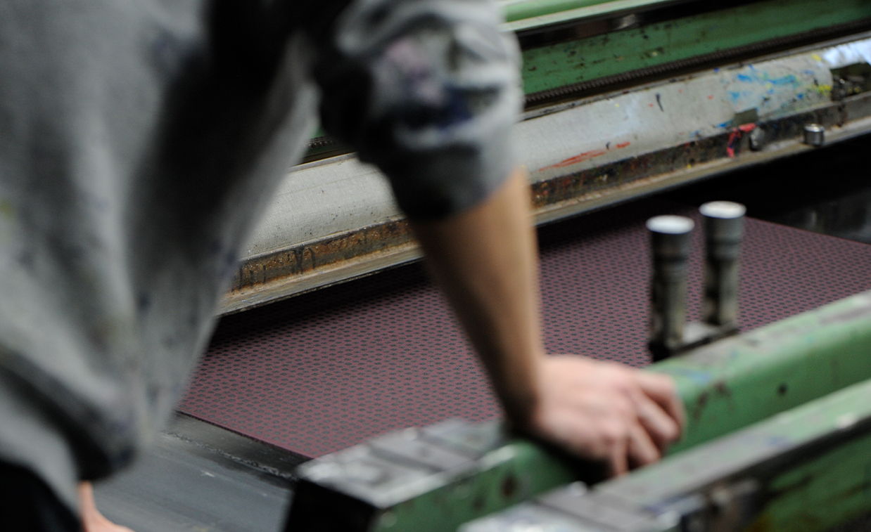 Person operating a printing press with a maroon surface.
