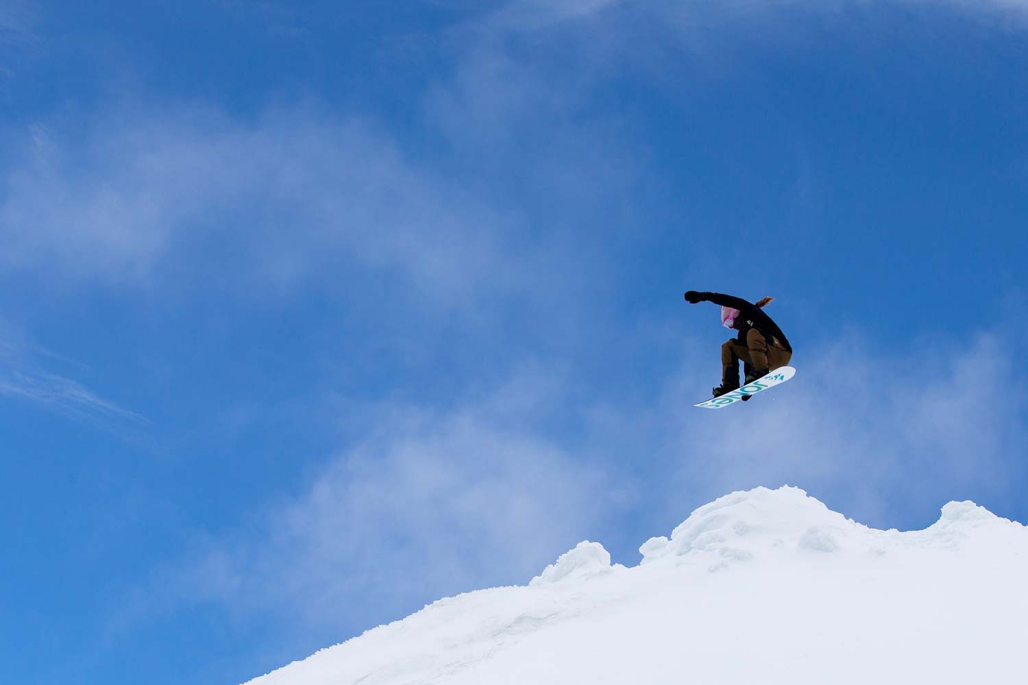 A snowboarder jumping off a snowy peak against a blue sky.
