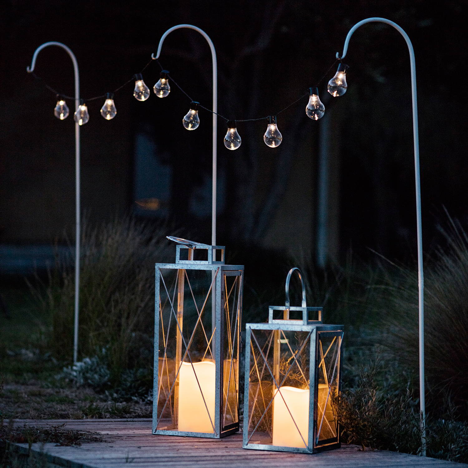 Festoon lights hanging on festoon poles in an outdoor setting with solar lanterns beneath them.