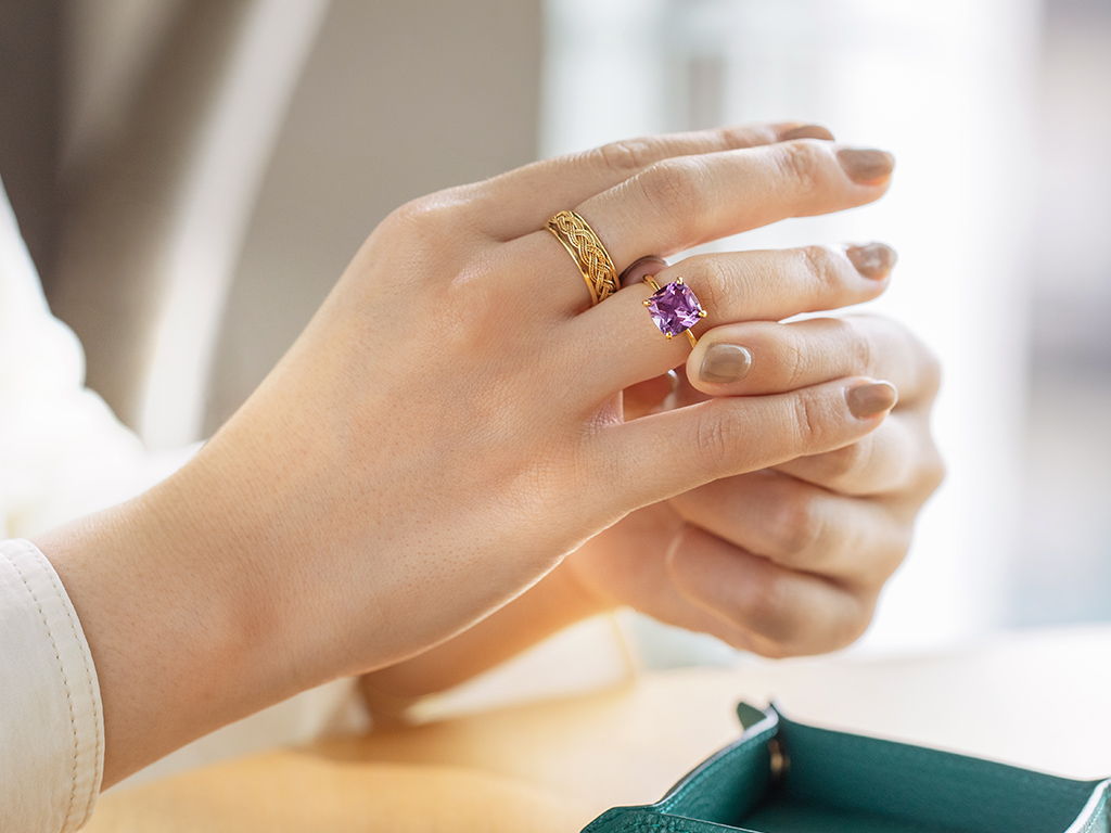 A close-up of a hand wearing multiple rings on a wooden surface.