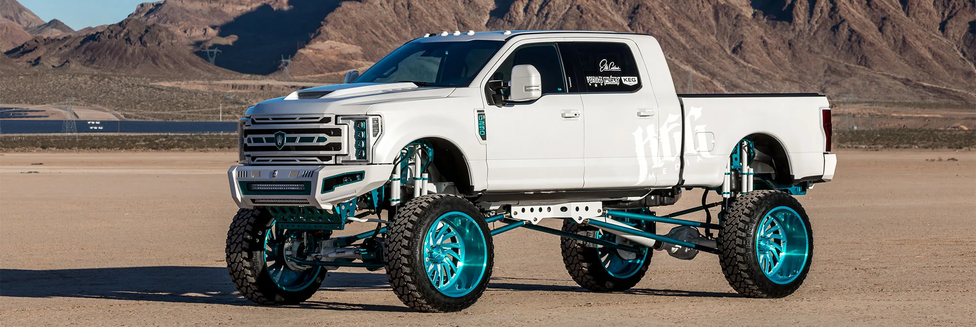 White Ford Super Duty lifted truck with teal suspension in desert
