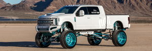 White Ford Super Duty lifted truck with teal suspension in desert