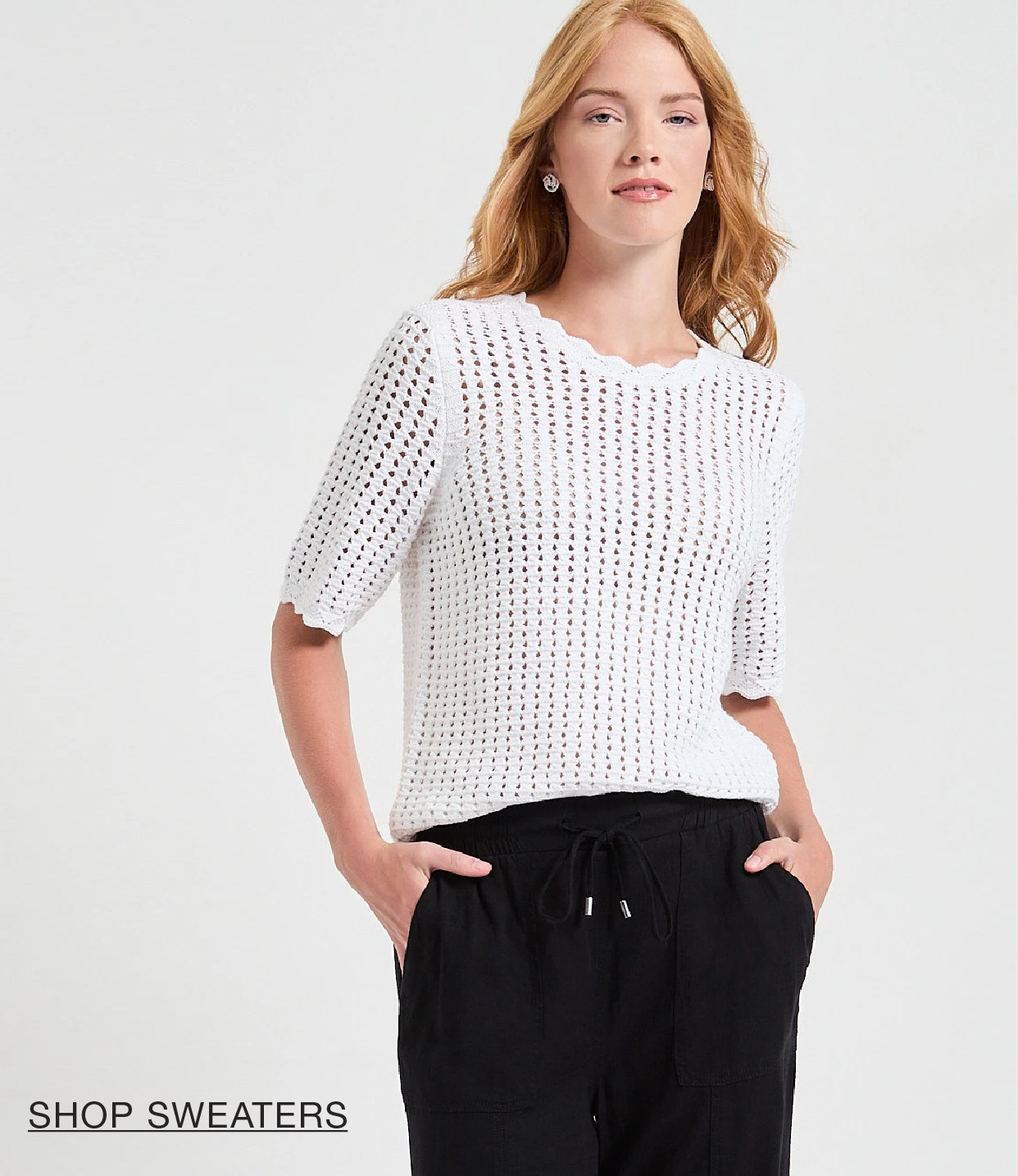 Woman wearing a white knit sweater and black pants, posing confidently.