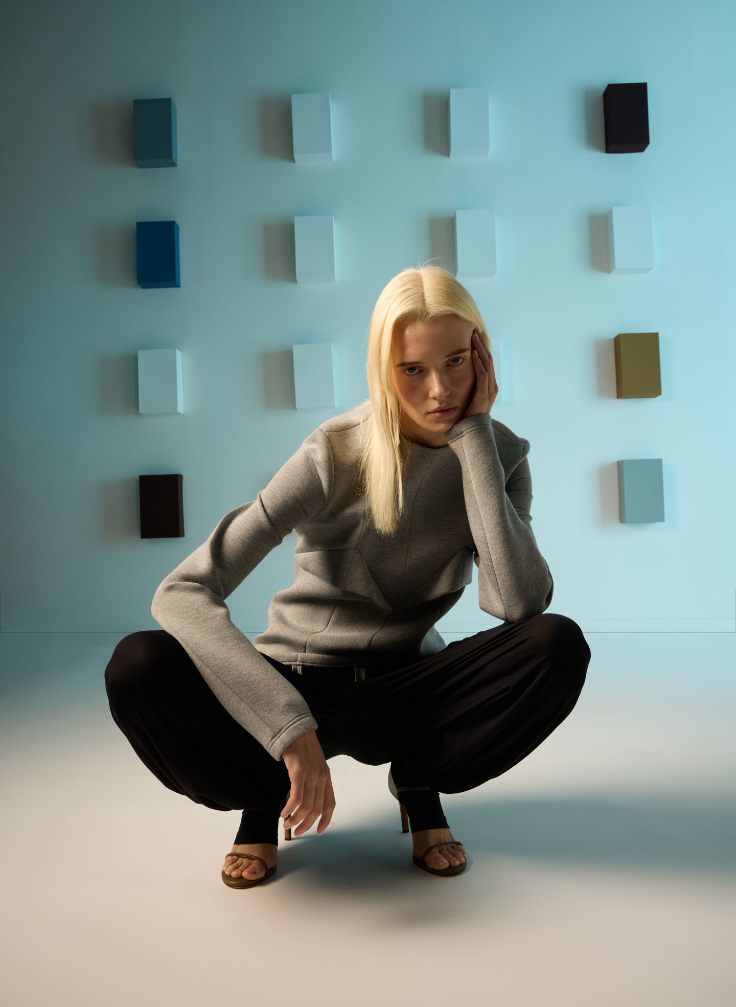A person squatting in front of colorful wall squares.