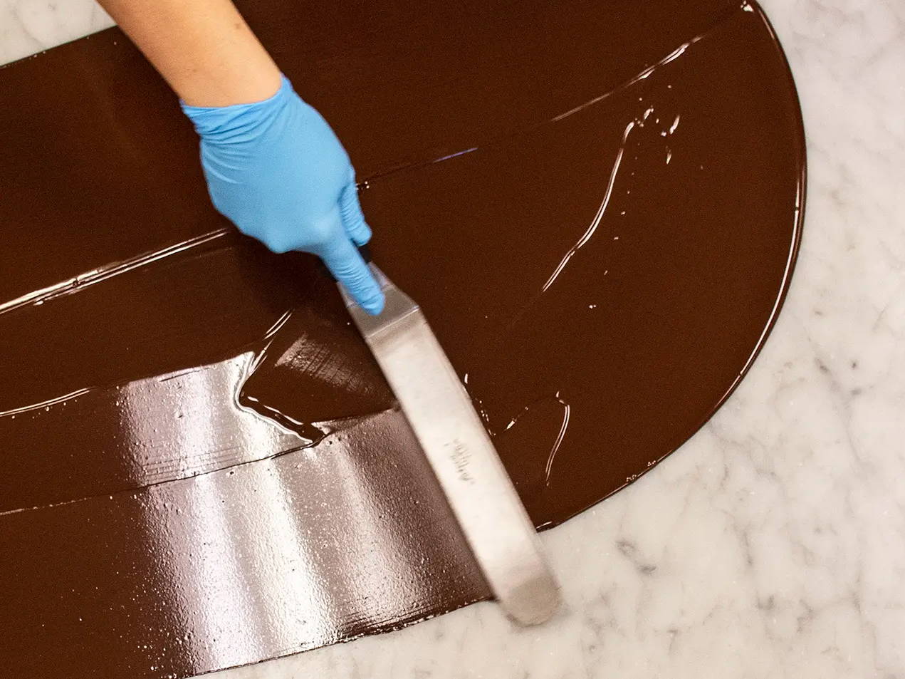Chocolatier's hand tempering melted chocolate on a marble counter top
