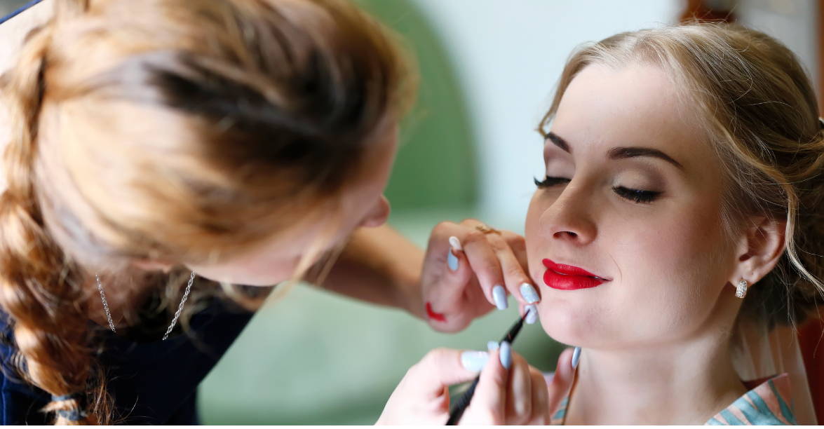 Bride having bright red lipstick applied by professional makeup artist.