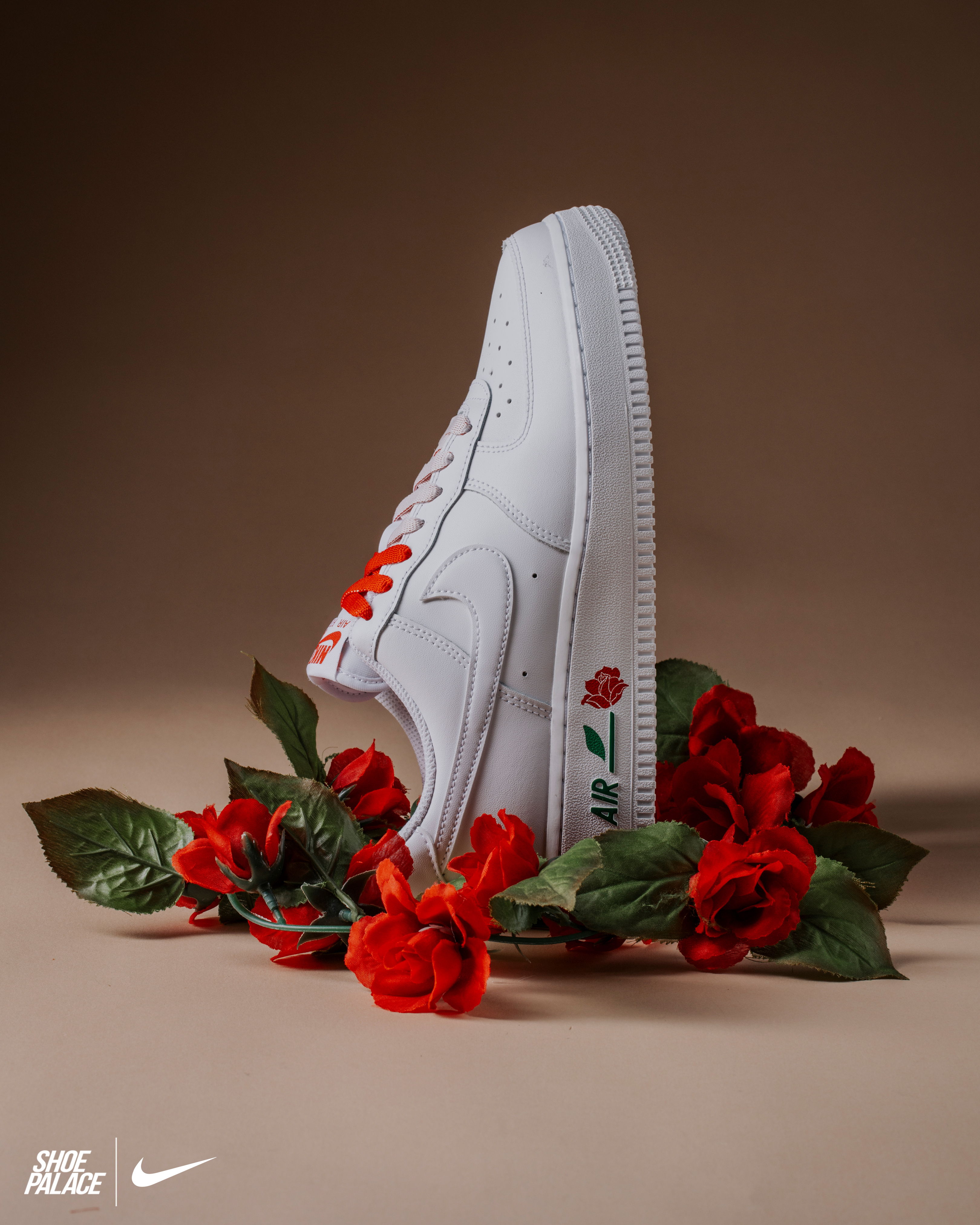 White Nike sneakers surrounded by red flowers and green leaves.