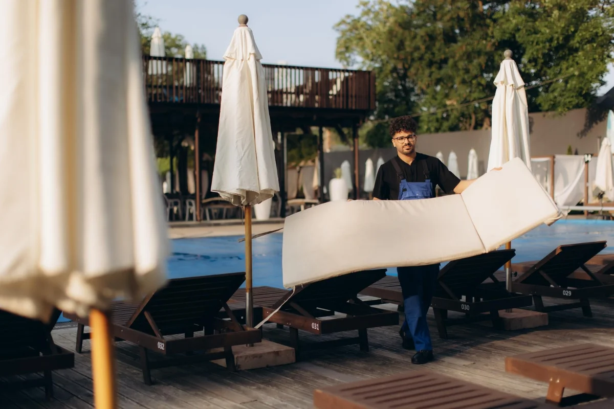 Hotel pool staff moving outdoor cushions from commercial lounge furniture as part of hospitality maintenance