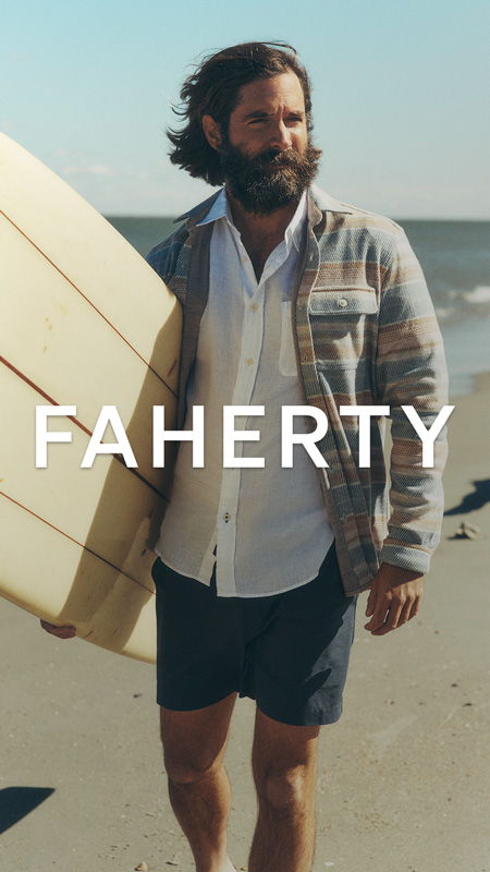 Man walking on beach holding surfboard, wearing casual clothing.