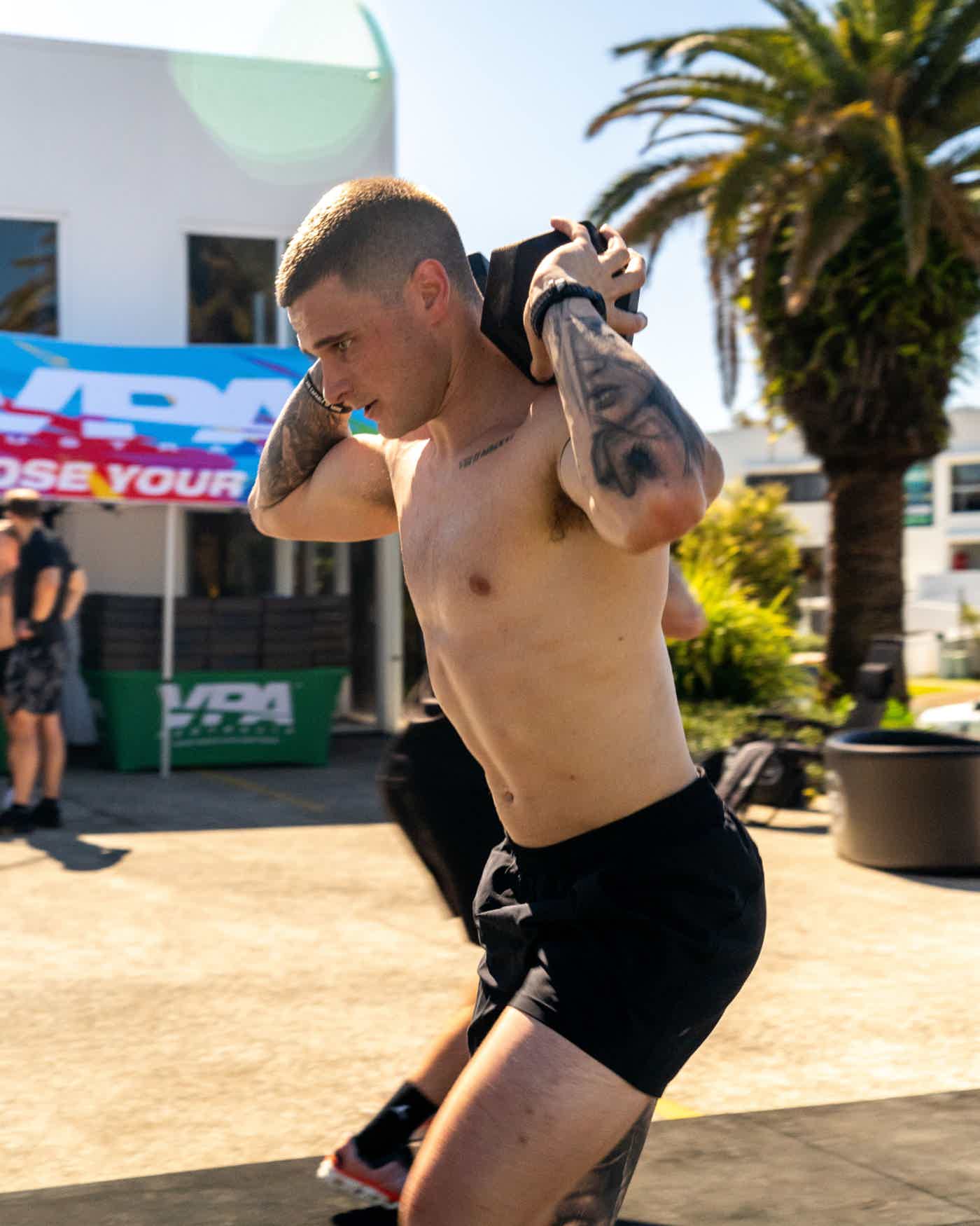A shirtless man exercising outdoors with palm trees in the background.