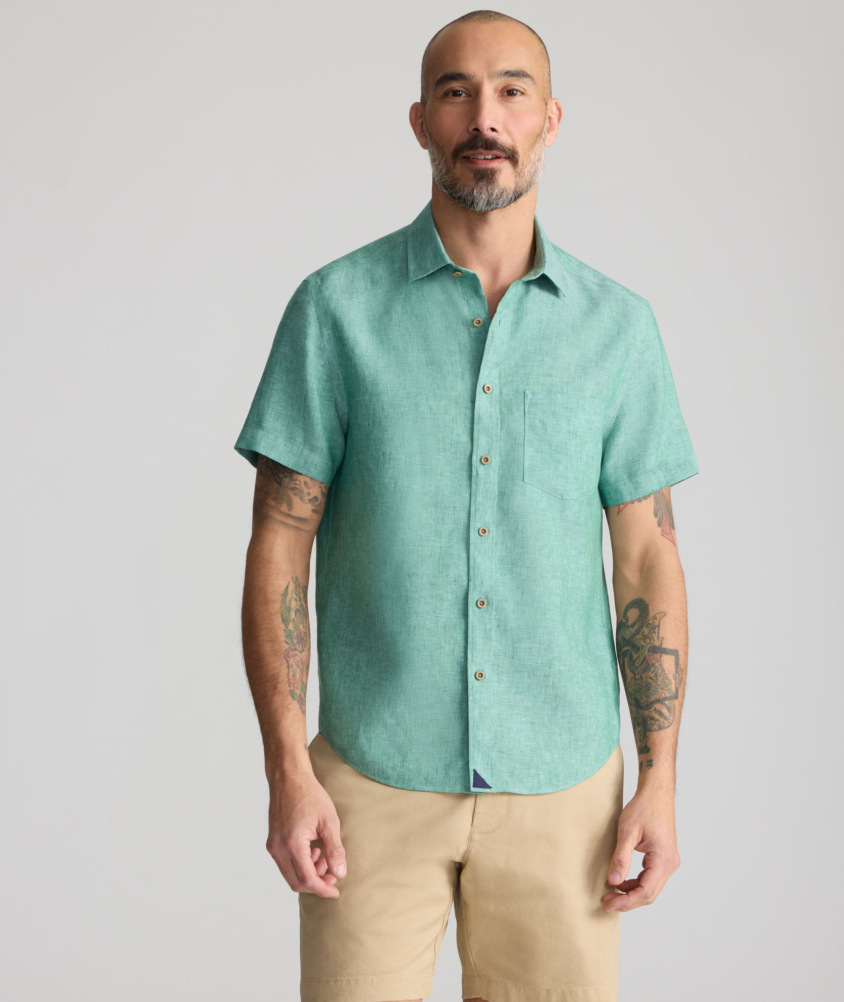 Man wearing a green short-sleeve shirt and beige pants, standing neutrally.