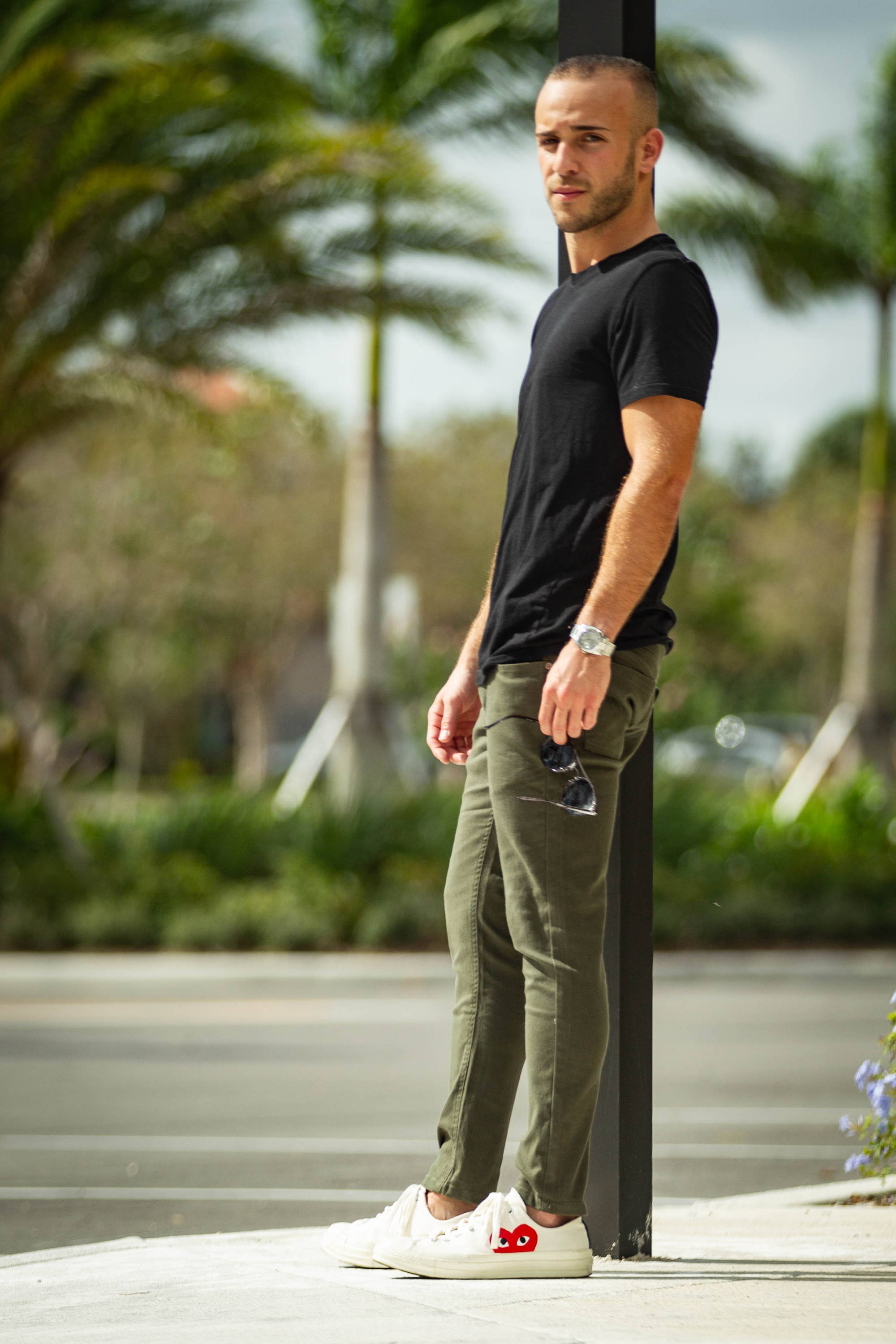 Man standing on sidewalk wearing white shoes, a black t shirt and olive green chinos from Under510.com