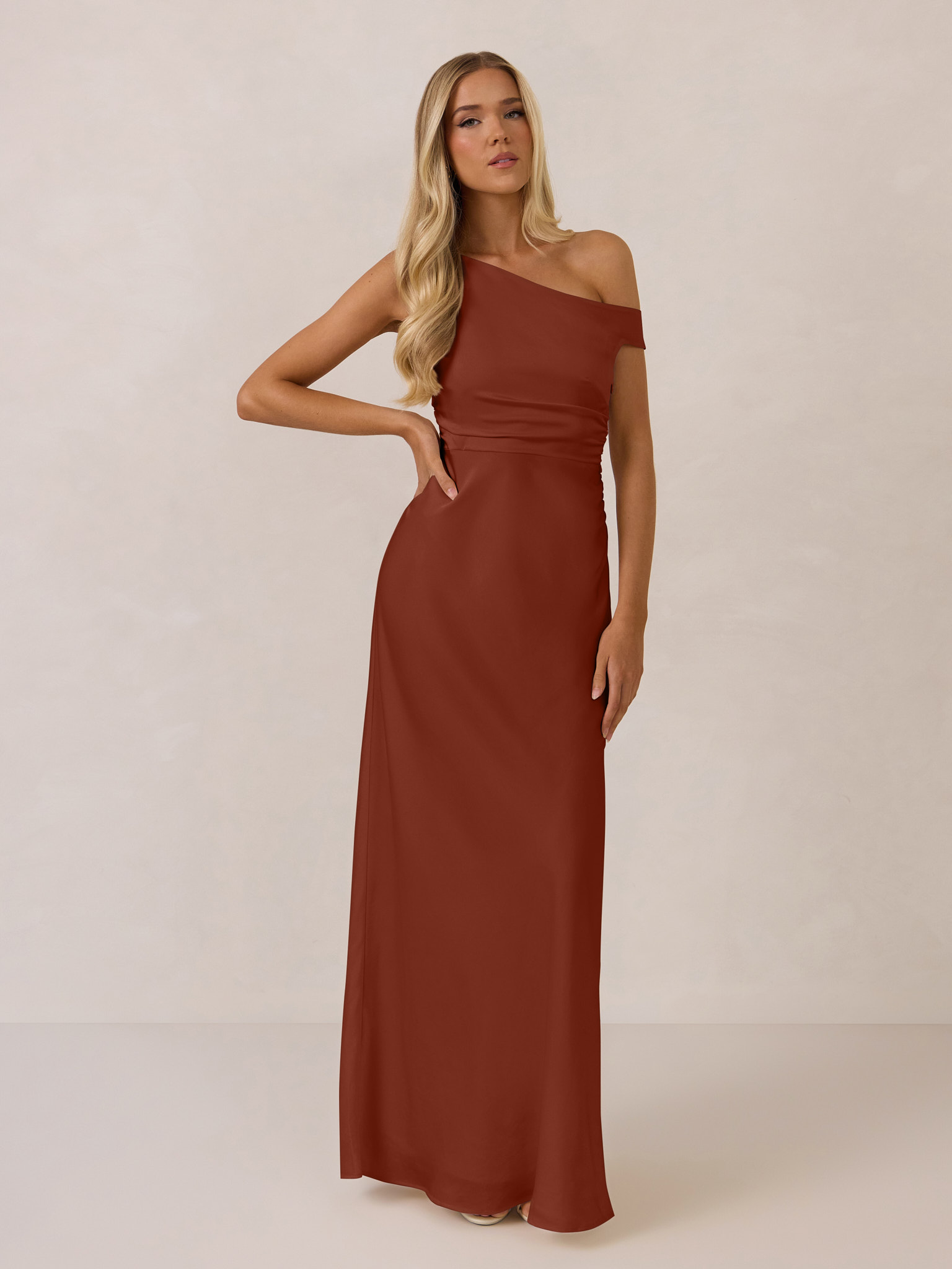 A woman in a rust-colored off-shoulder dress poses elegantly.