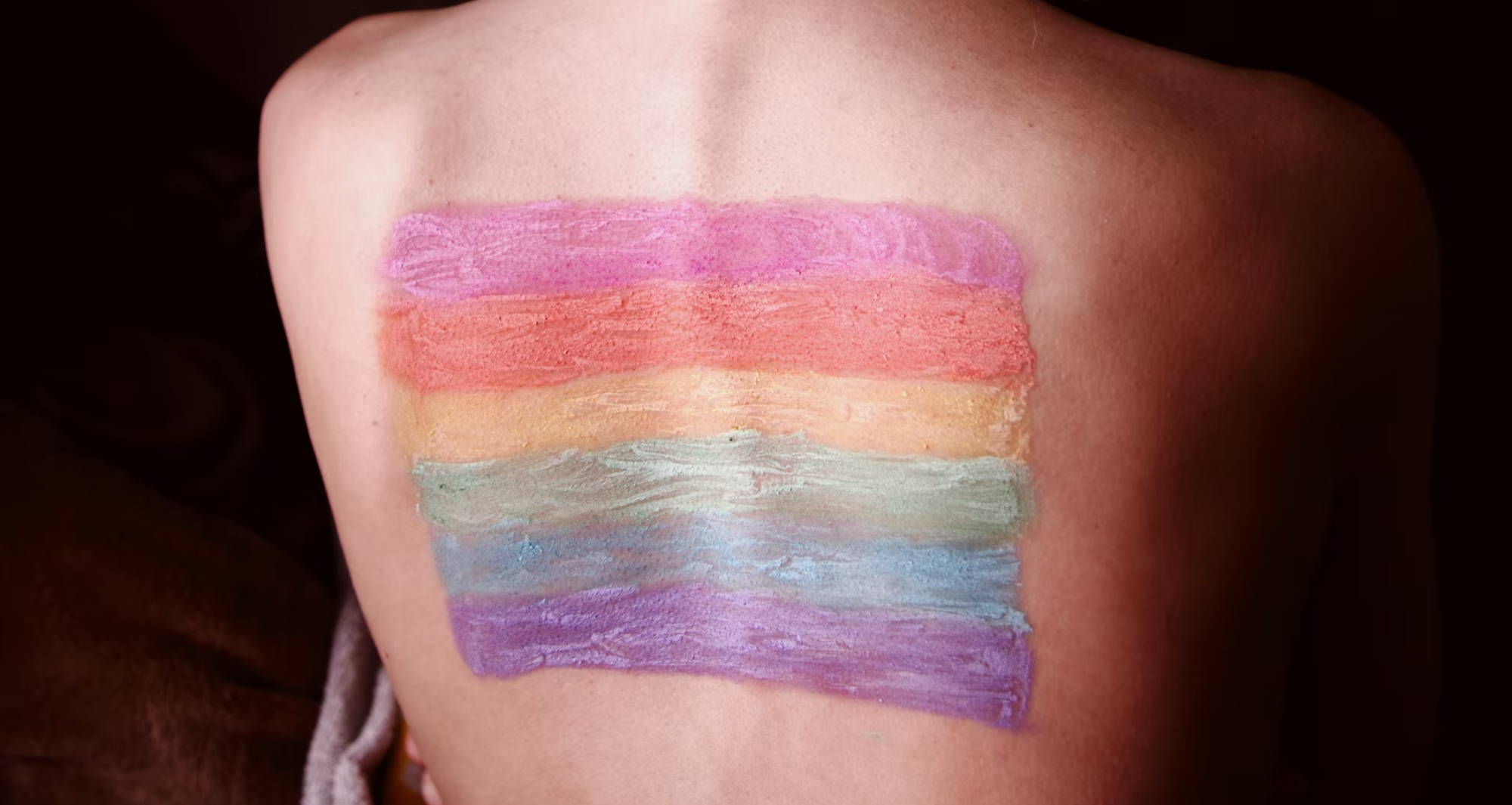  woman’s back with scoliosis with a rainbow flag painted on it