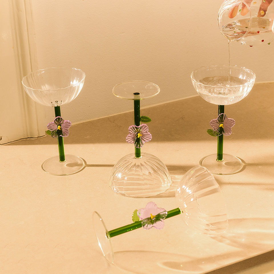 Four decorative glasses with green stems and purple flowers on a surface.