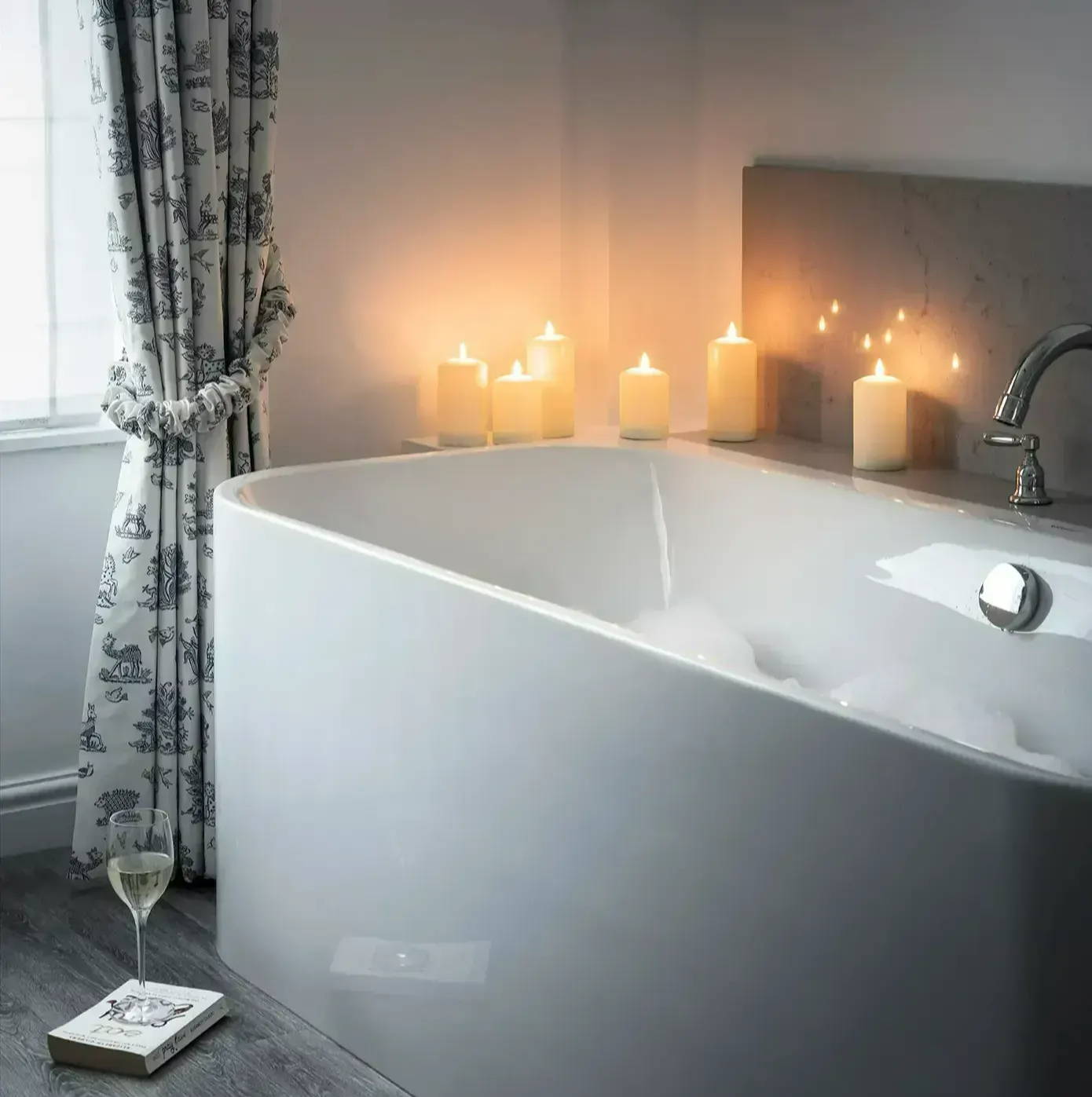 A photo of a bubble bath with TruGlow candles a glass of wine and a book.