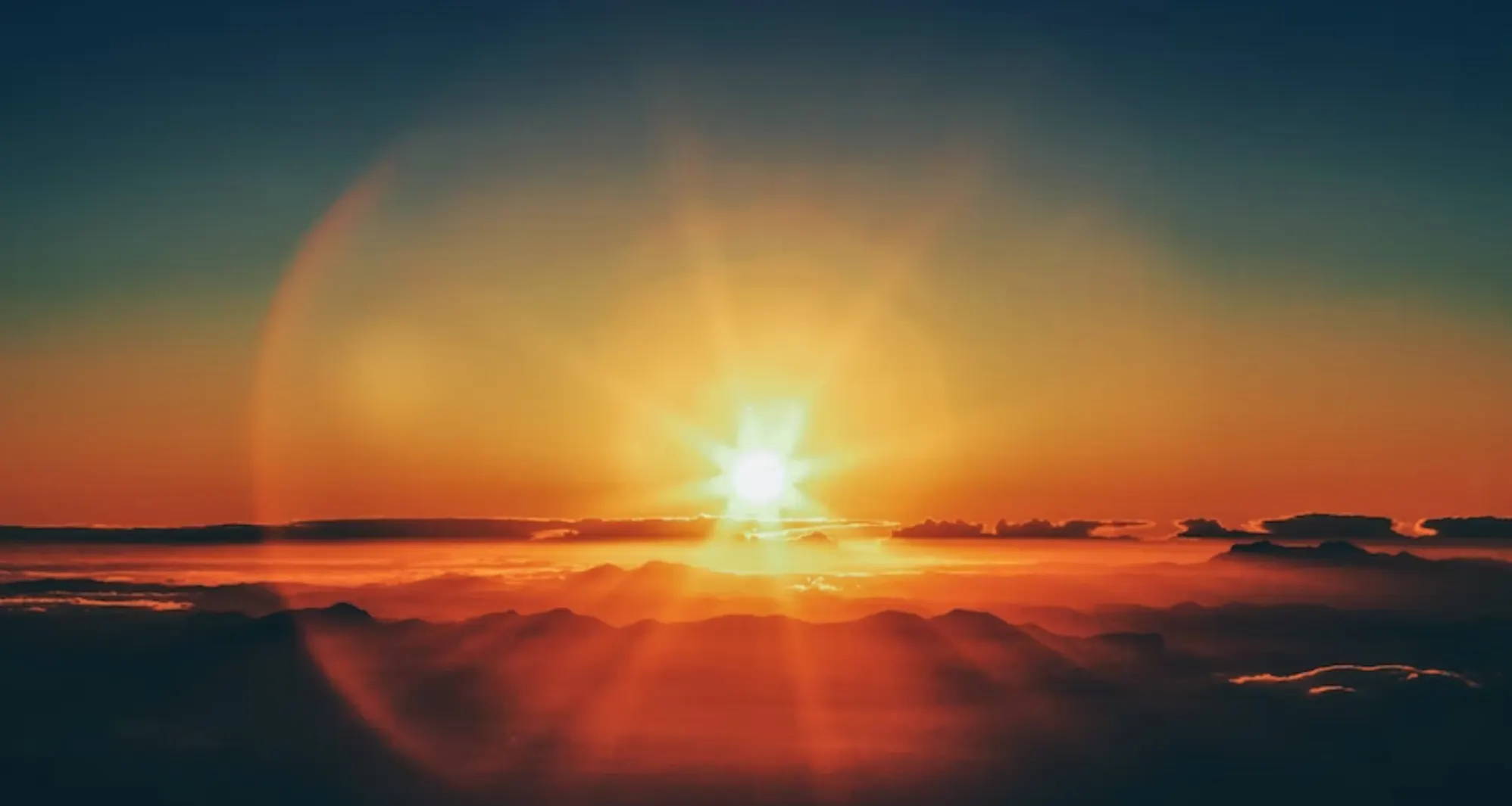 A bright orange sunset over a mountain range and amongst dark clouds.