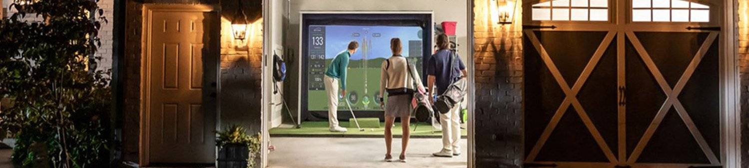 Golfers playing on a SkyTrak home golf simulator in their garage setup