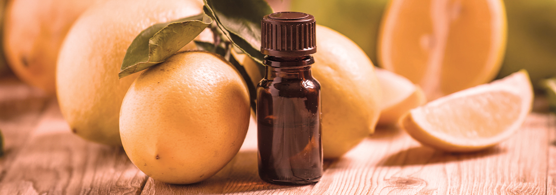 Bottle of essential oil with fresh lemons on a wooden surface.