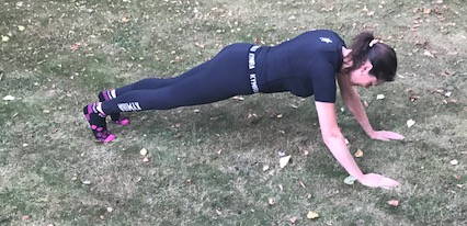 A woman in a plank position with her hands on the grass.