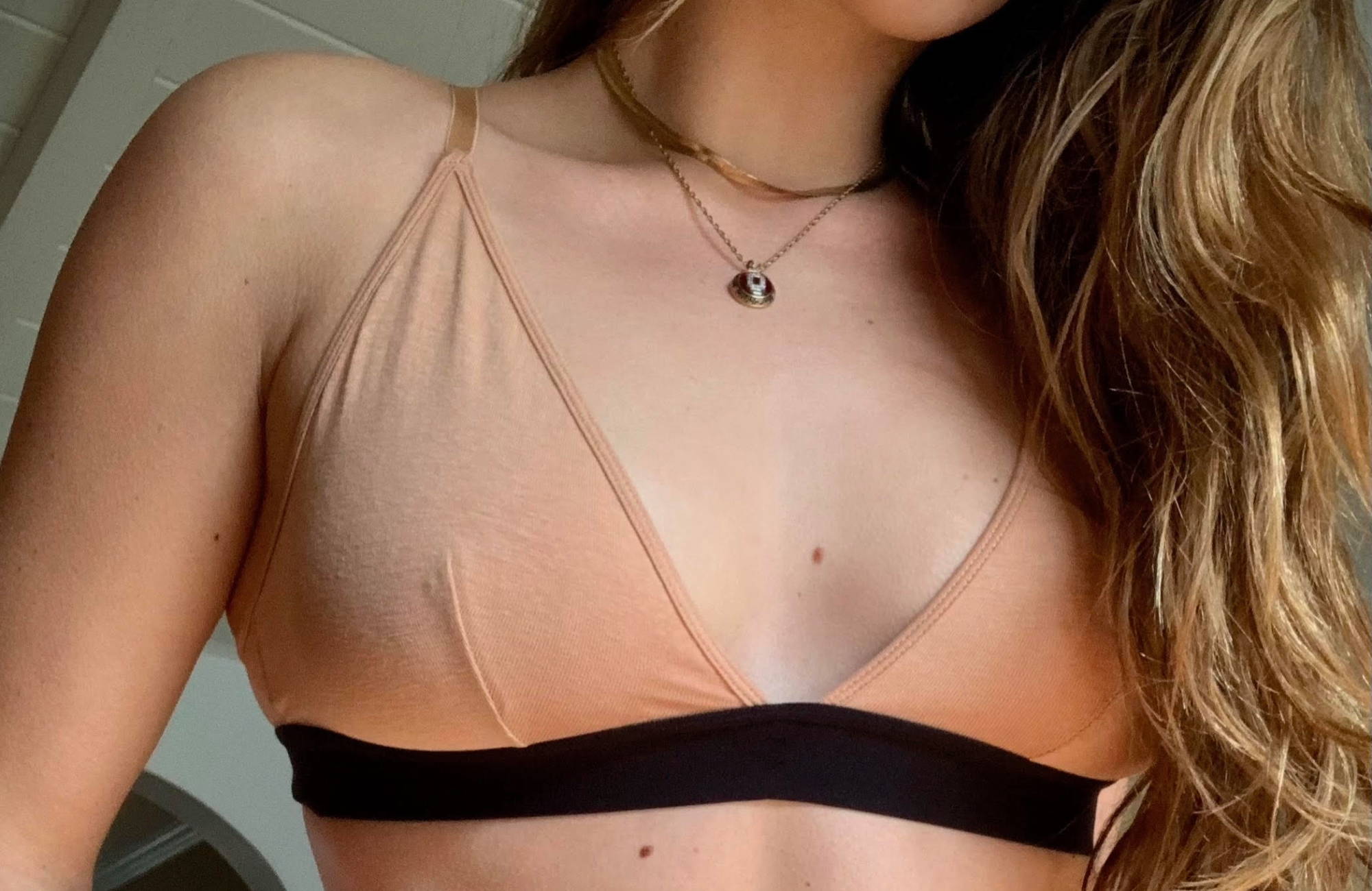 close up of a nude triangle bralette on a woman with long light brown hair flowing over one shoulder with two short necklaces