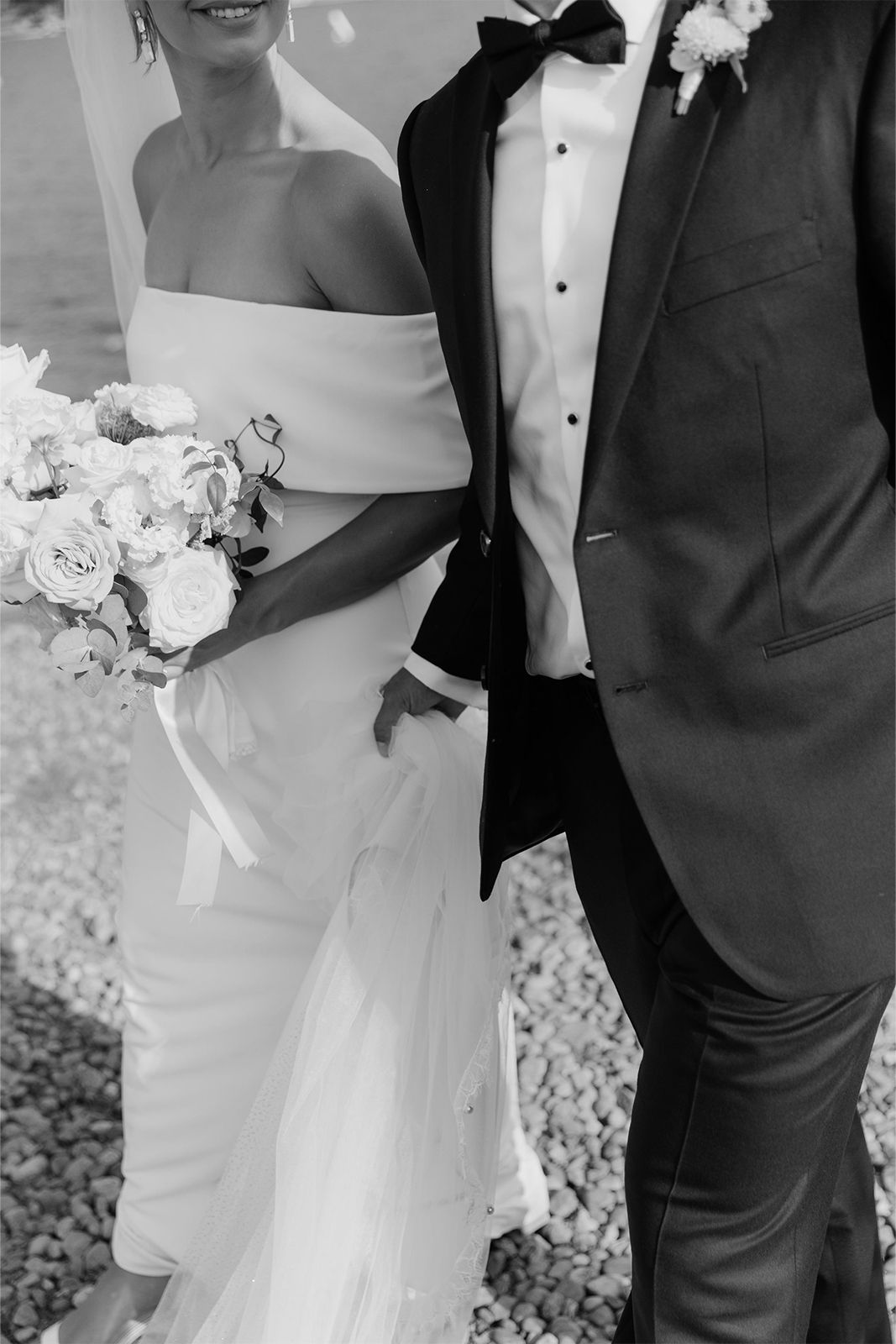 A smiling couple in formal attire, holding flowers, walking together.