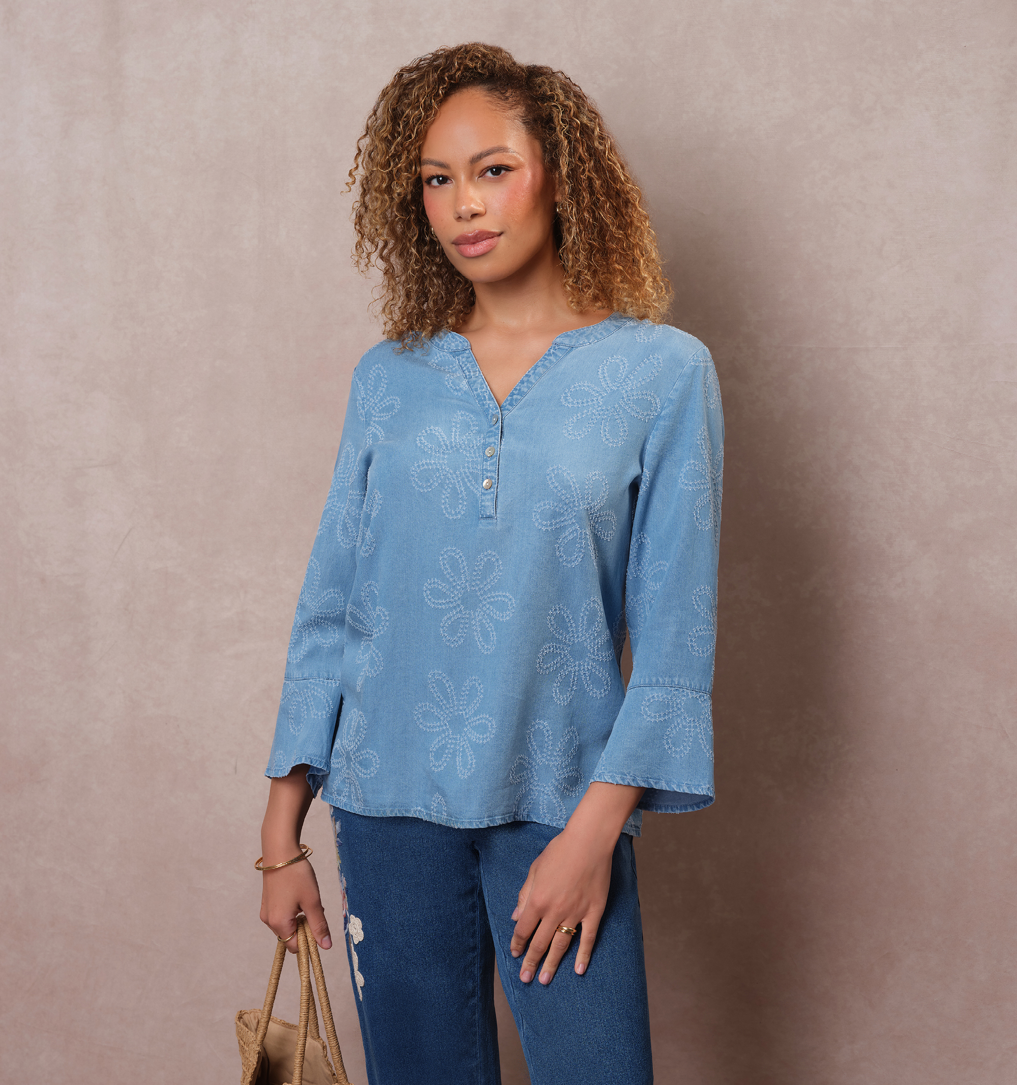 A person in a blue top and jeans against a neutral background.