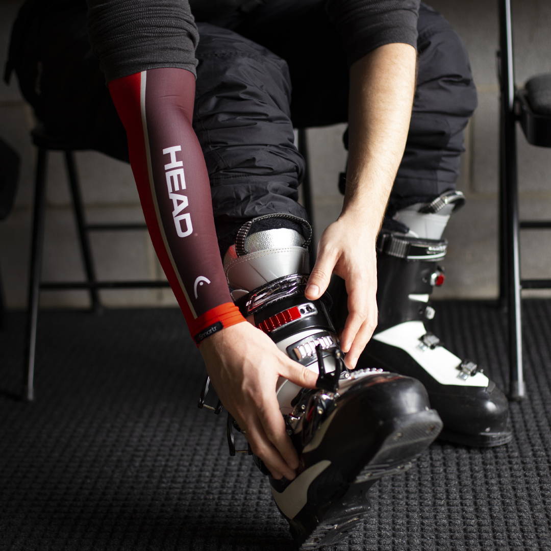 An athlete putting their ski boot on, wearing a HEAD smart compression sleeve.