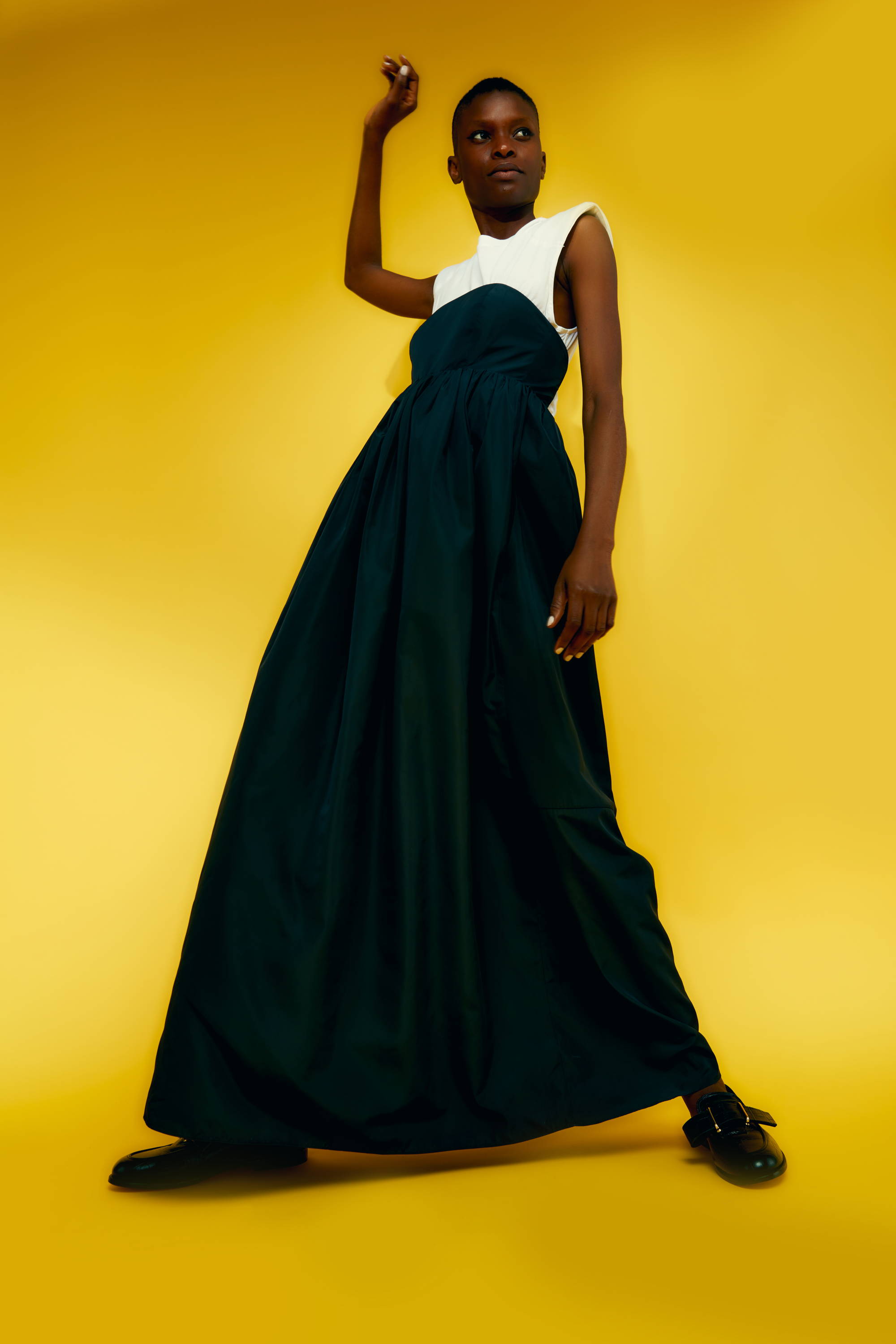 Model in a long, flowing dark dress against a bright yellow background.